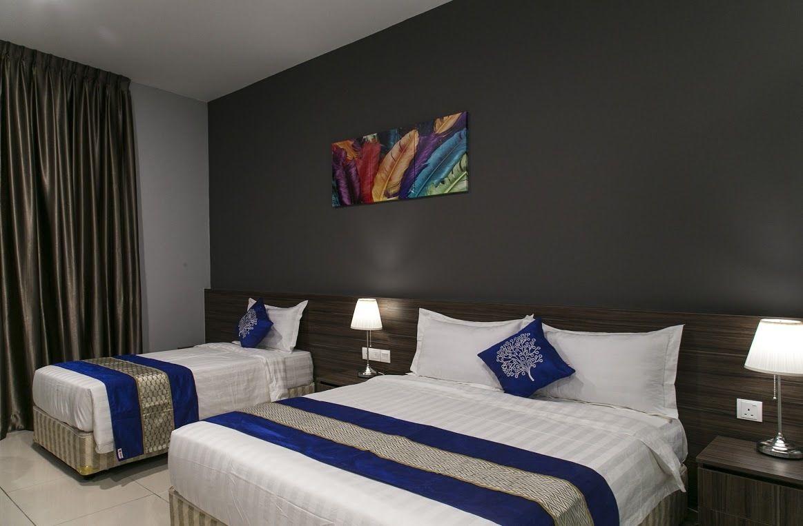 Une chambre d’hôtel avec deux lits, chacun recouvert d’une couvre-lit bleue et blanche, dotés d’une tête de lit en bois foncé et agrémentée d’un tableau accroché au mur.