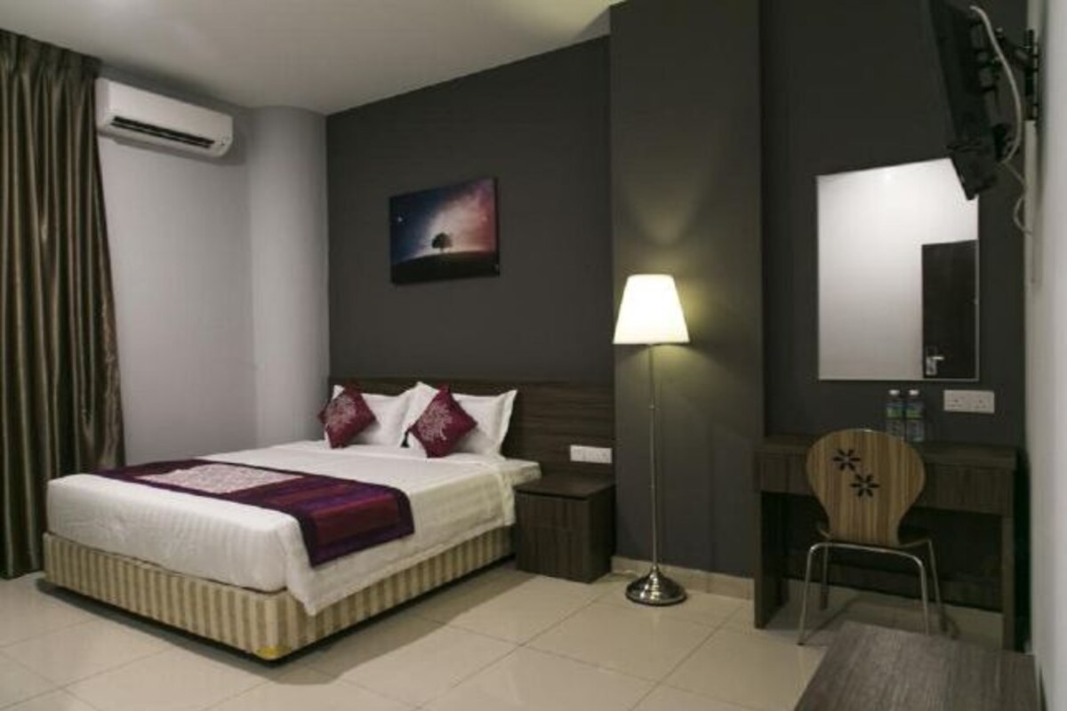 Une chambre d’hôtel équipée d’un lit, d’une table de chevet, d’une lampe, d’une chaise, d’un bureau, d’un miroir et d’un appareil de climatisation.