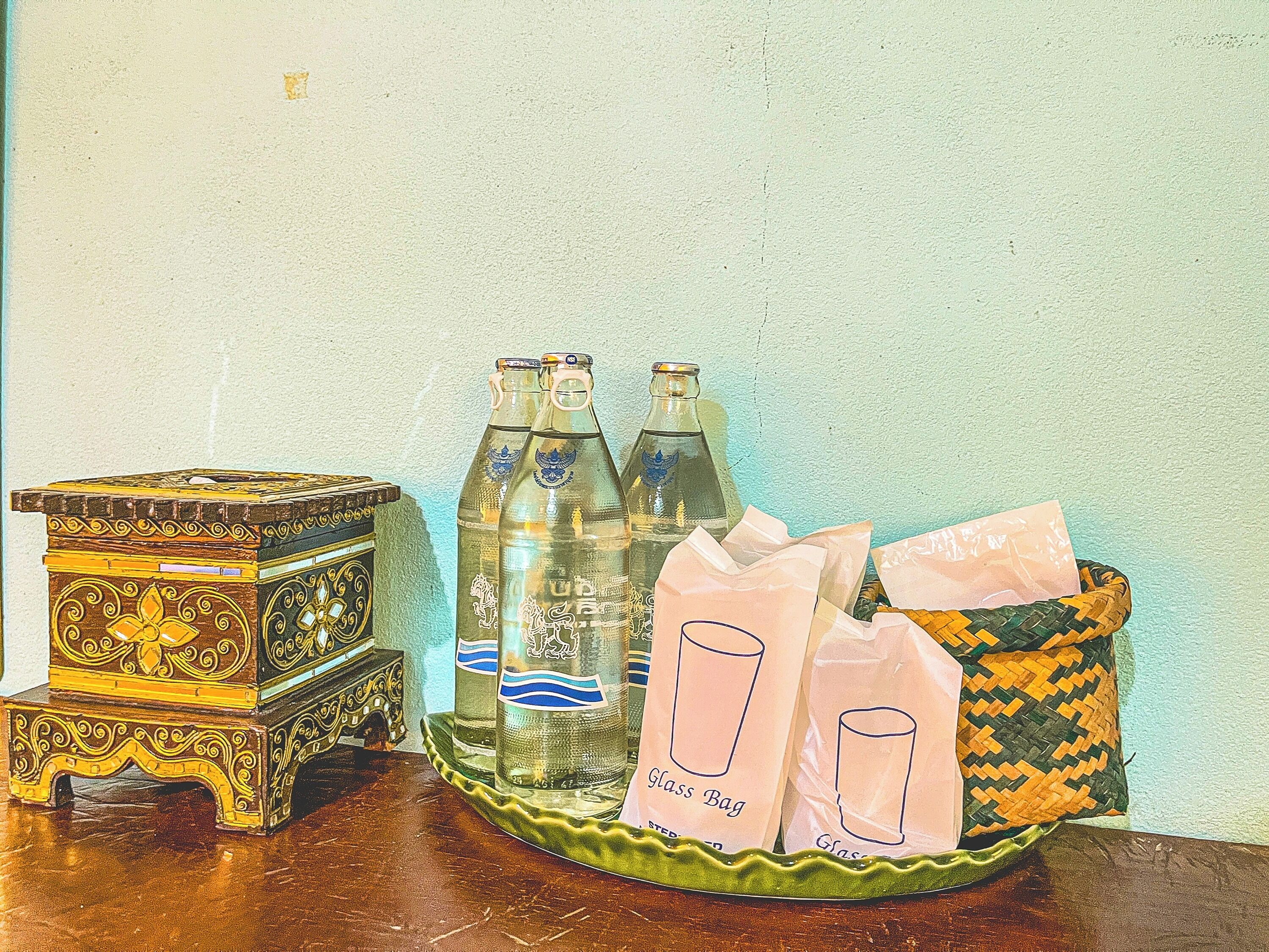 A wooden chest with intricate carvings, two glass bottles with labels, and two glass bags with labels on a wooden table against a textured wall.