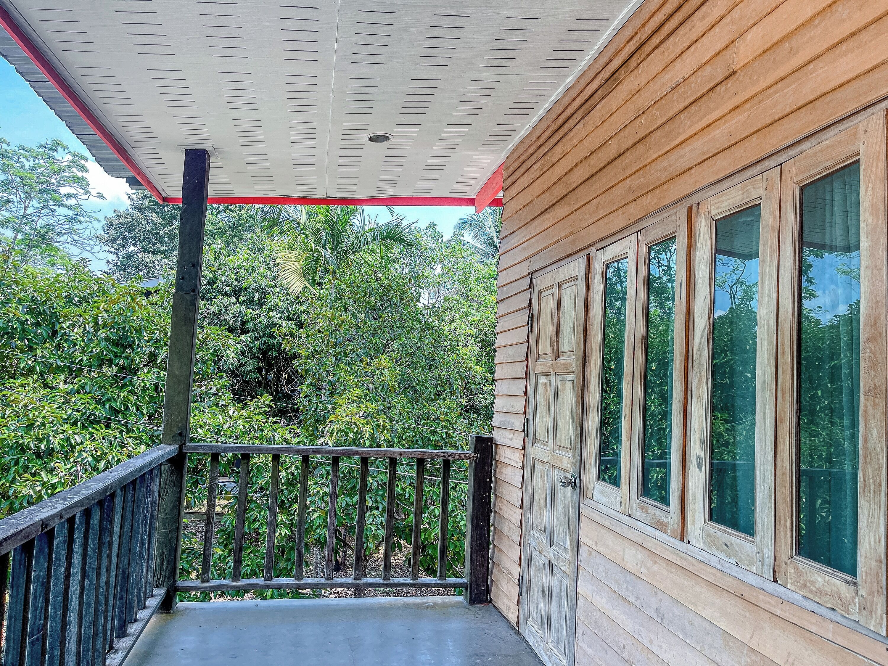 A wooden house with a balcony, large windows, and a red roof.