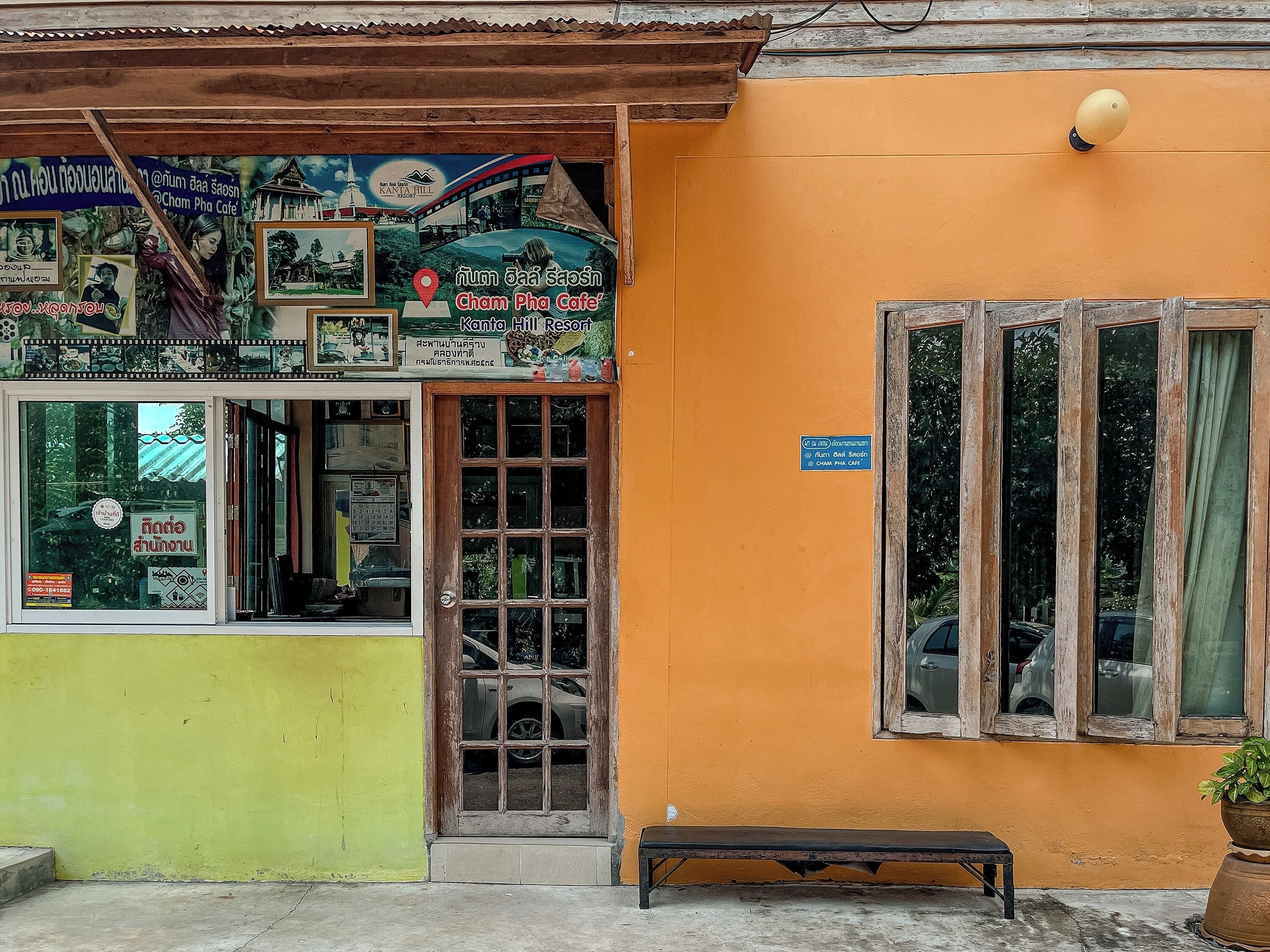 A building with a green and orange facade, a wooden door, and a bench outside.