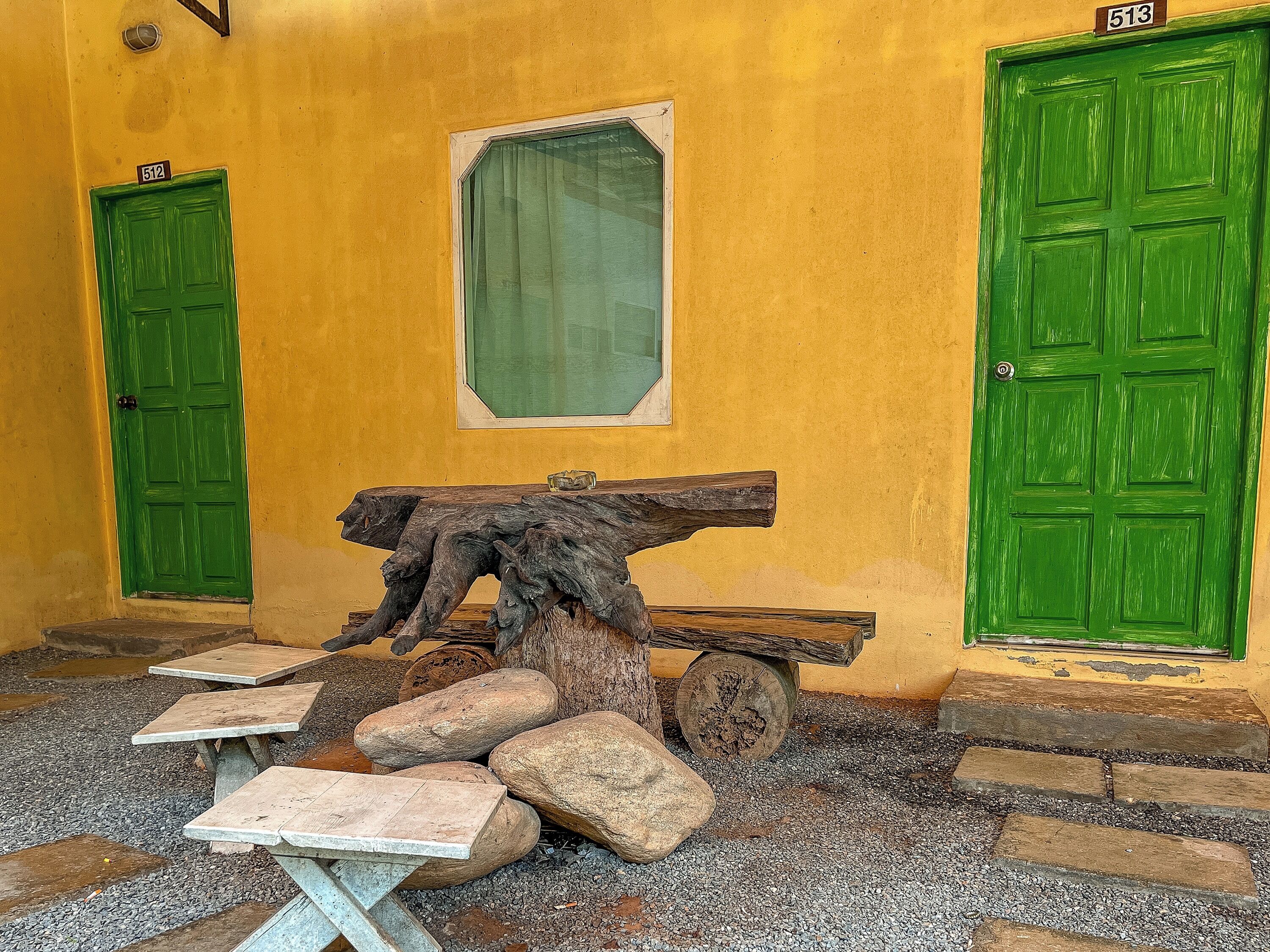 A room with two green doors, one labeled 512 and the other 513, a wooden table with a rustic centerpiece, and a small window with a green curtain.