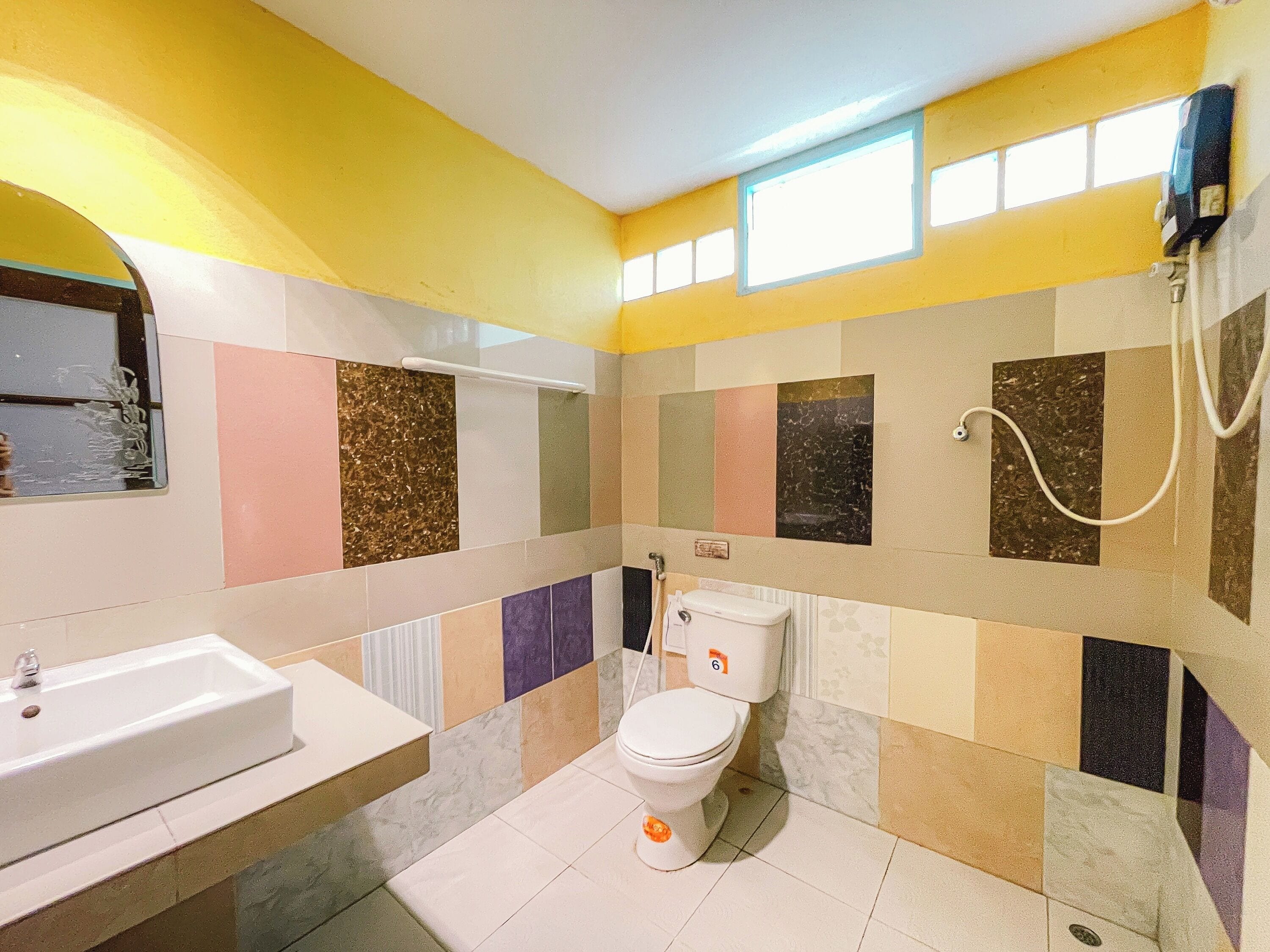 Et badeværelse med en hvid vask, toilet og bruseniche. Væggene er dekoreret med mosaikfliser.