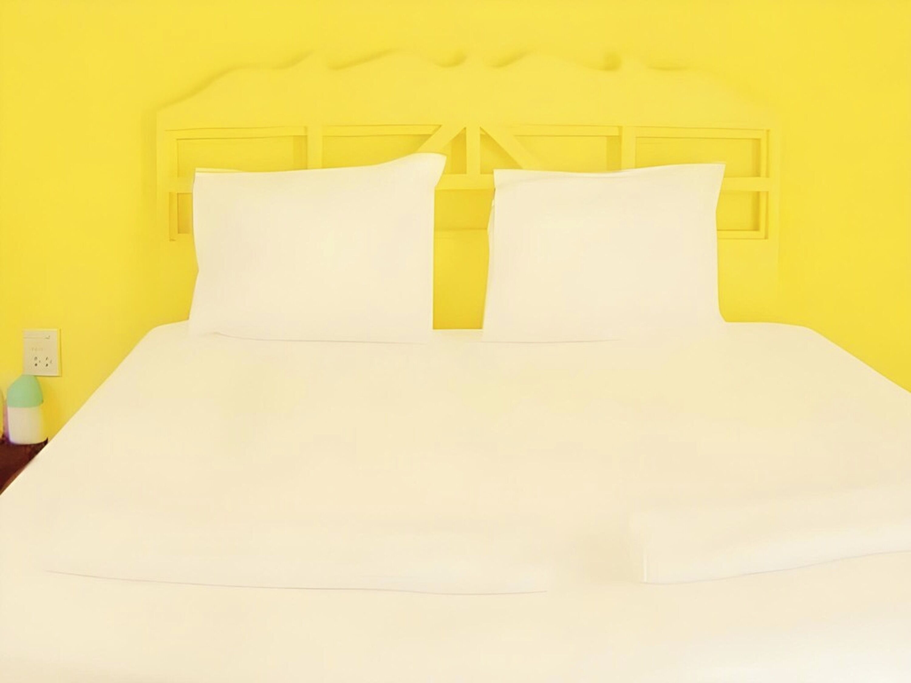A bed with a white mattress and pillows, set against a yellow wall.