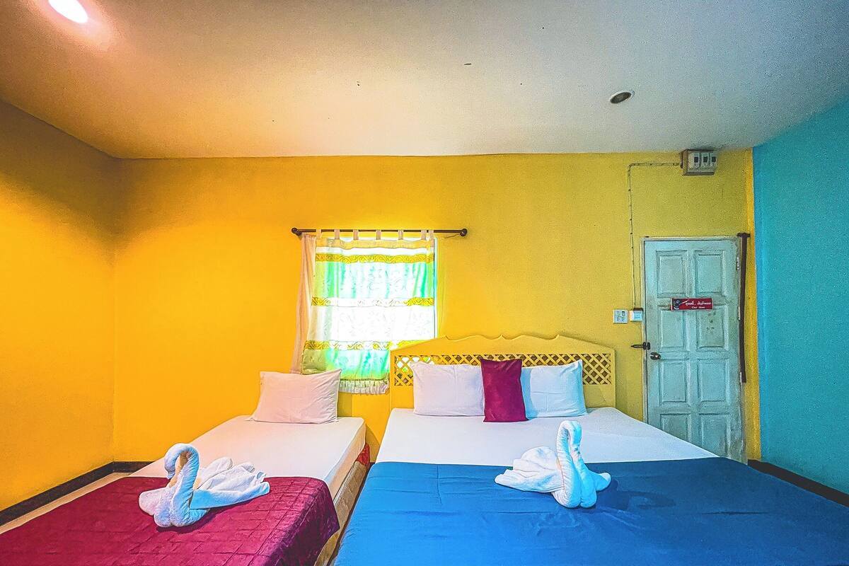 A room with two beds, each with a different colored bedspread, a window with curtains, and a door with a sign.