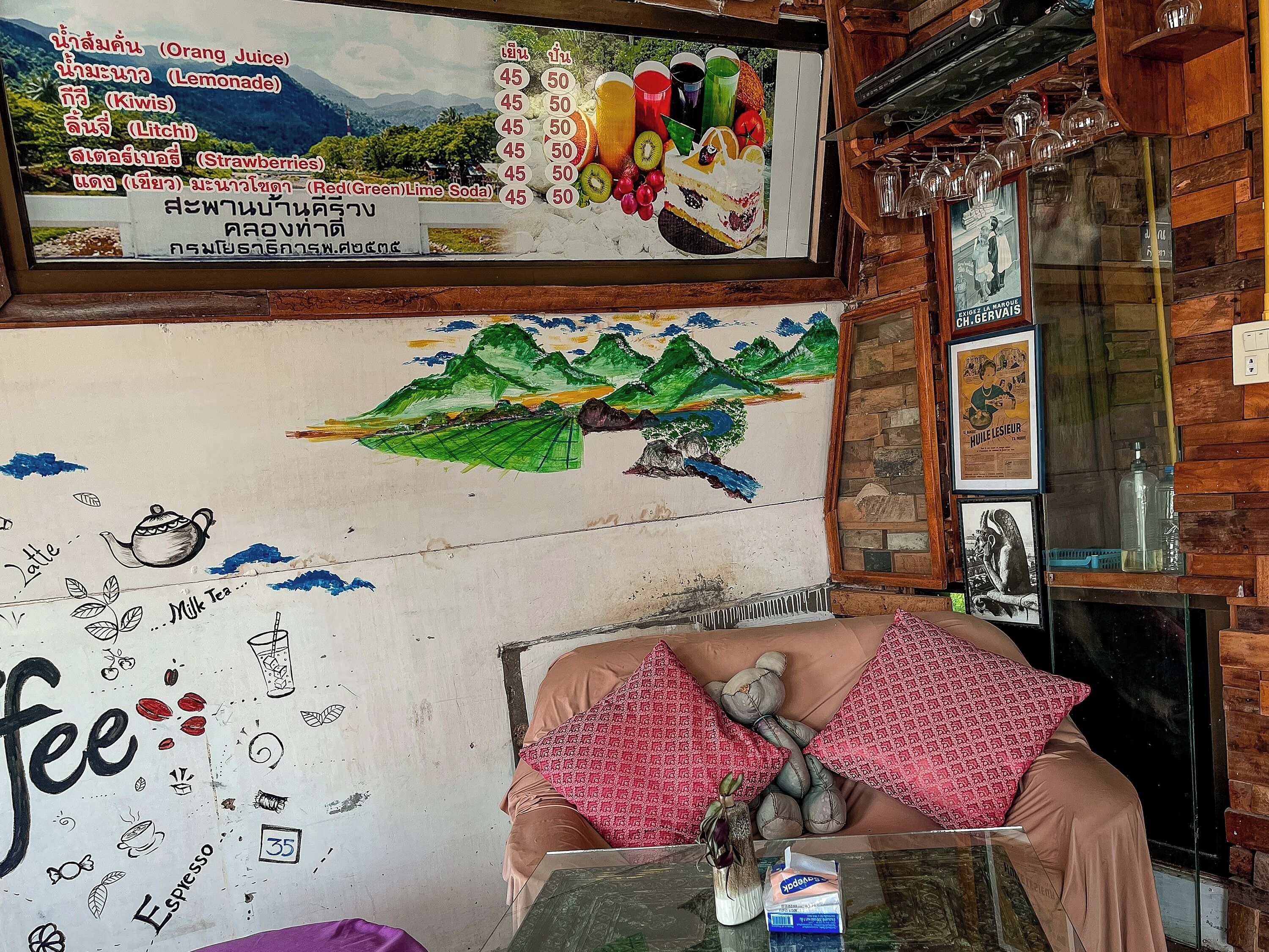 A room with a mural of mountains, a table with a vase, and a wall with a menu listing drinks and prices.