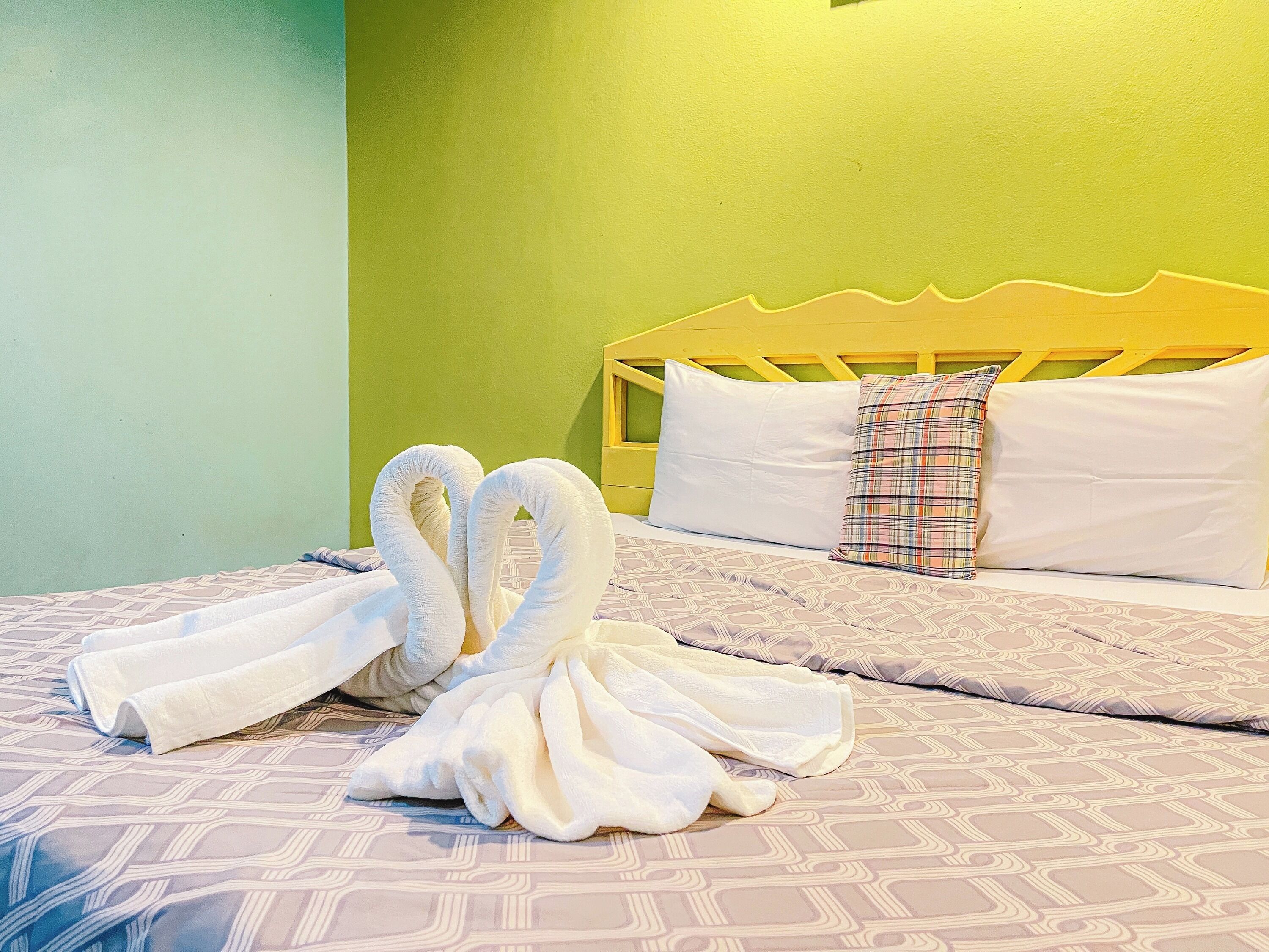 A bed with a patterned bedspread, a pillow with a plaid design, and two towels arranged in a swan shape.