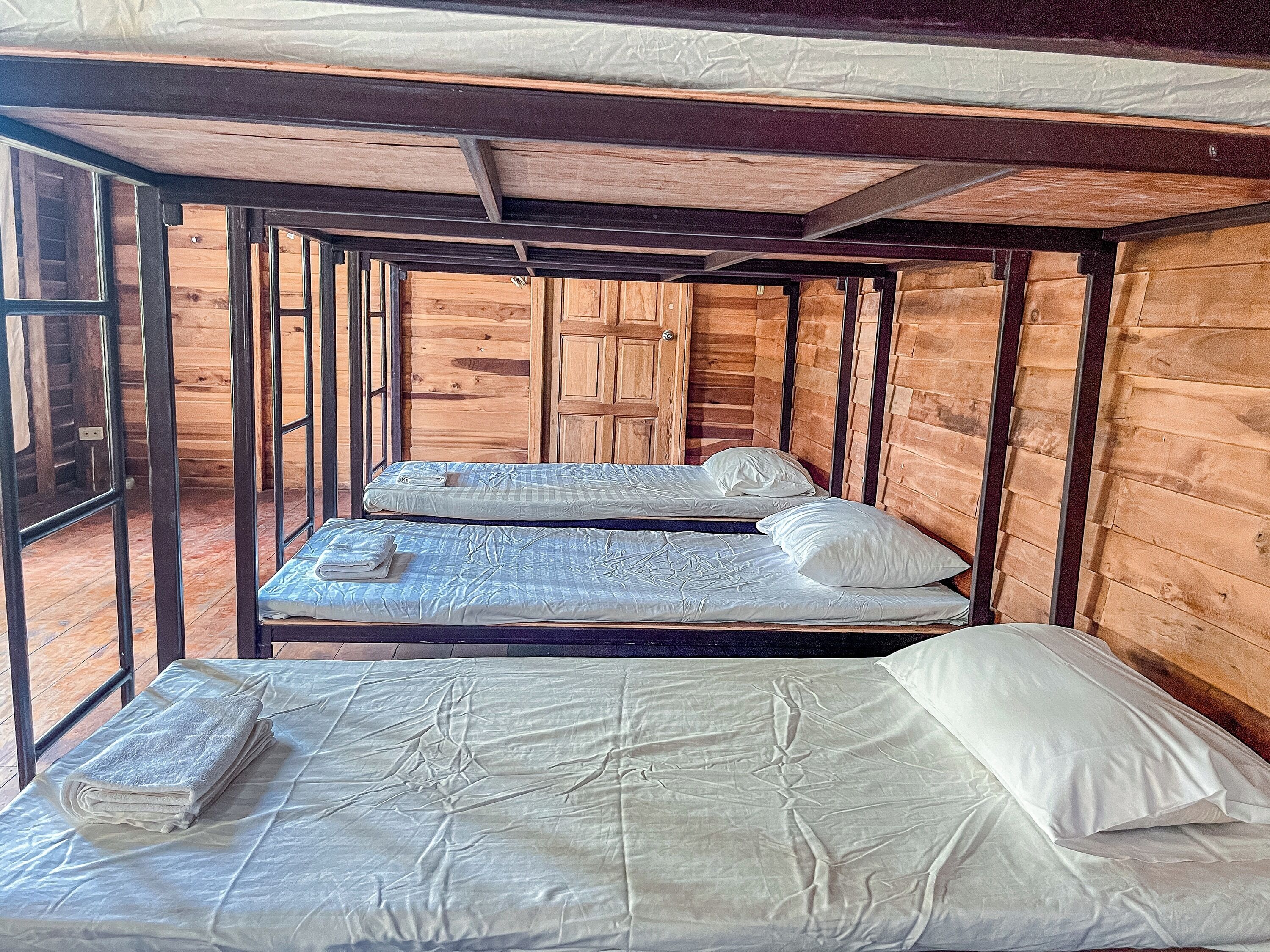A wooden cabin room with two beds, one with a folded blanket and the other with a rolled-up towel.