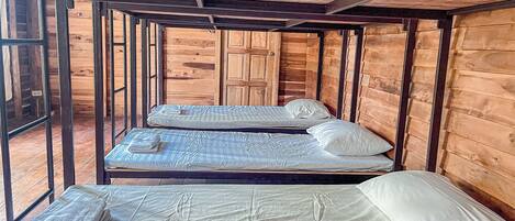 A wooden cabin room with two beds, one with a folded blanket and the other with a rolled-up towel.