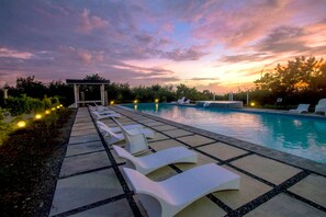 Un área de piscina con sillones reclinables y un pabellón.