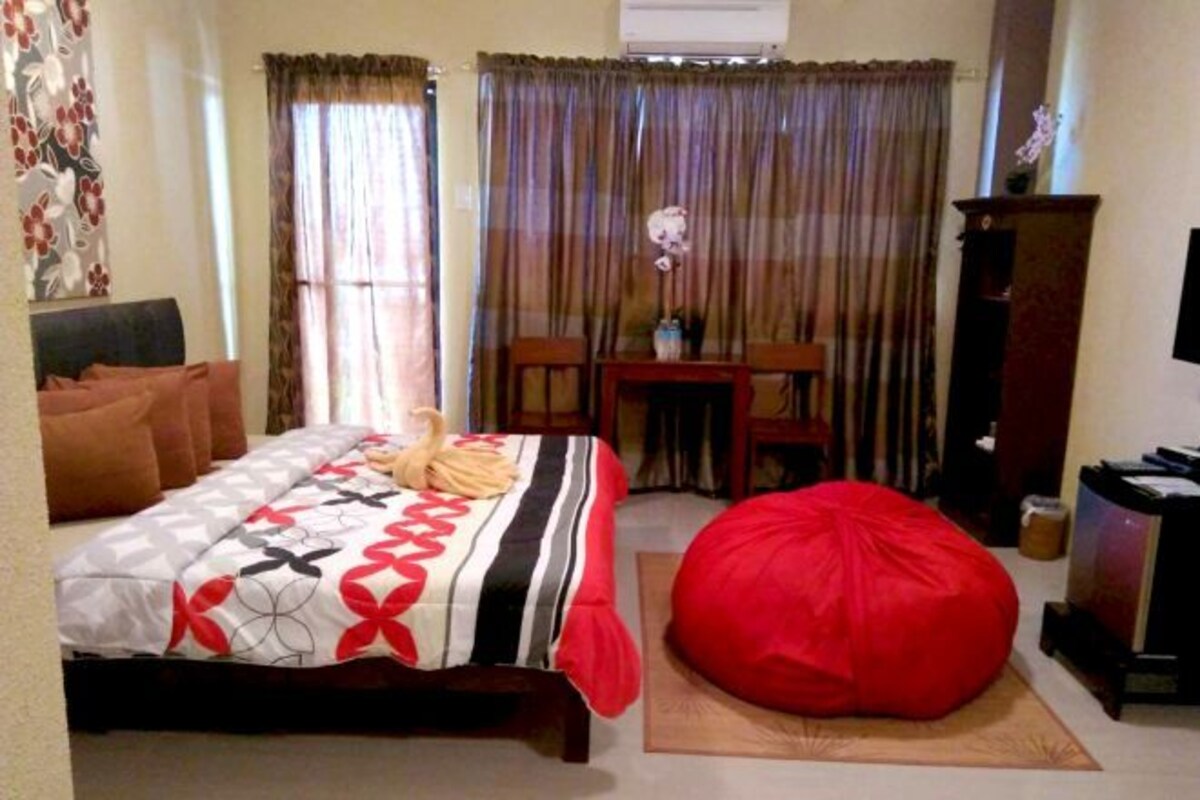 Un dormitorio con cama, un sillón de peluche rojo, un escritorio y una silla.