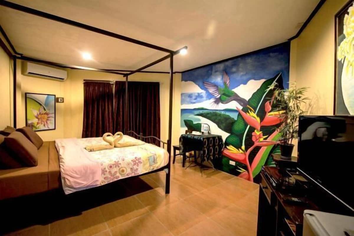 A room with a bed, a desk, a chair, a TV, and a mural on the wall.