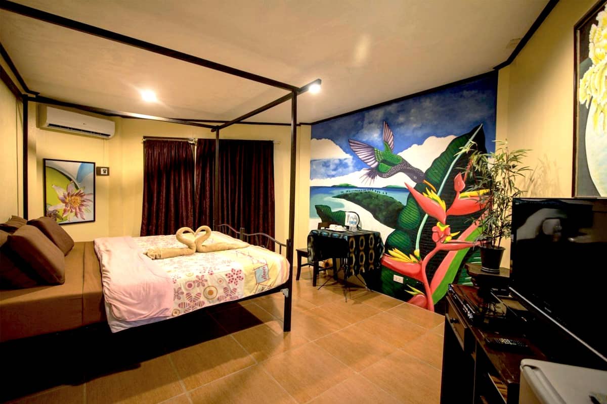 A hotel room with a bed, a desk, a television, and a mural on the wall.