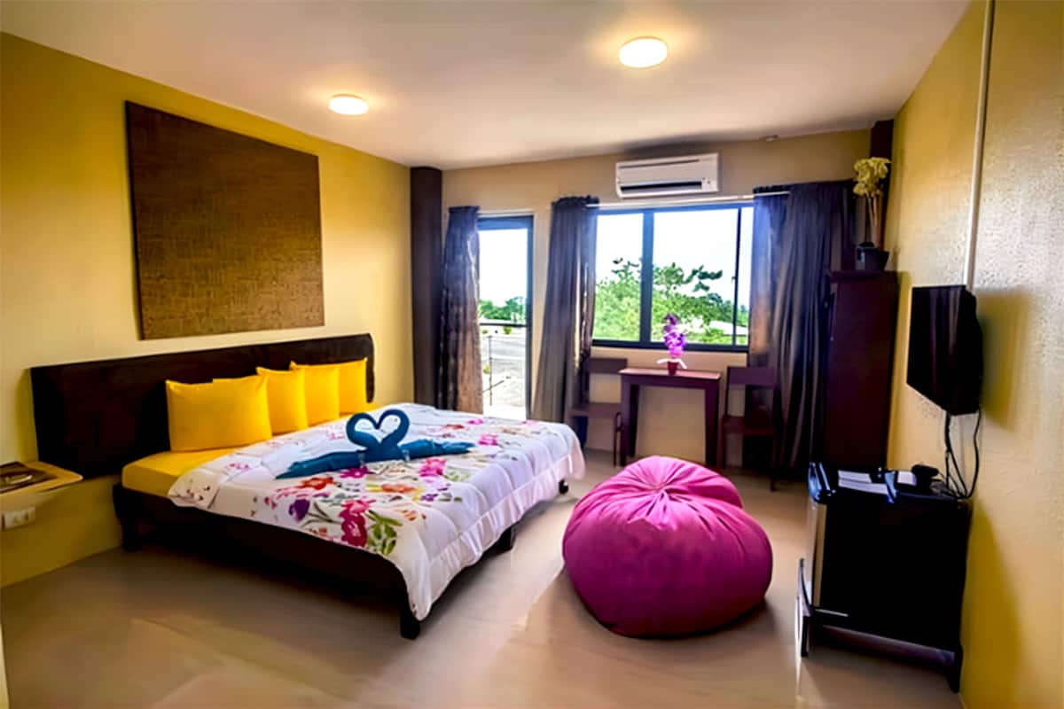 A hotel room with a bed, a desk, a chair, a television, and an air conditioning unit.