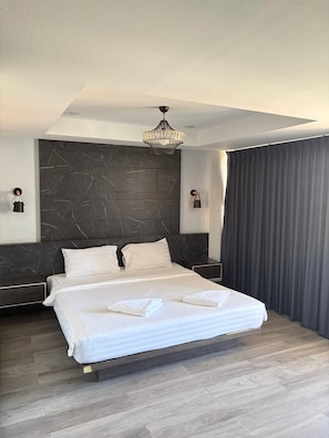A modern bedroom with a large bed, dark marble headboard, and a chandelier. - Palette Jomtien Longstay (Pattaya)