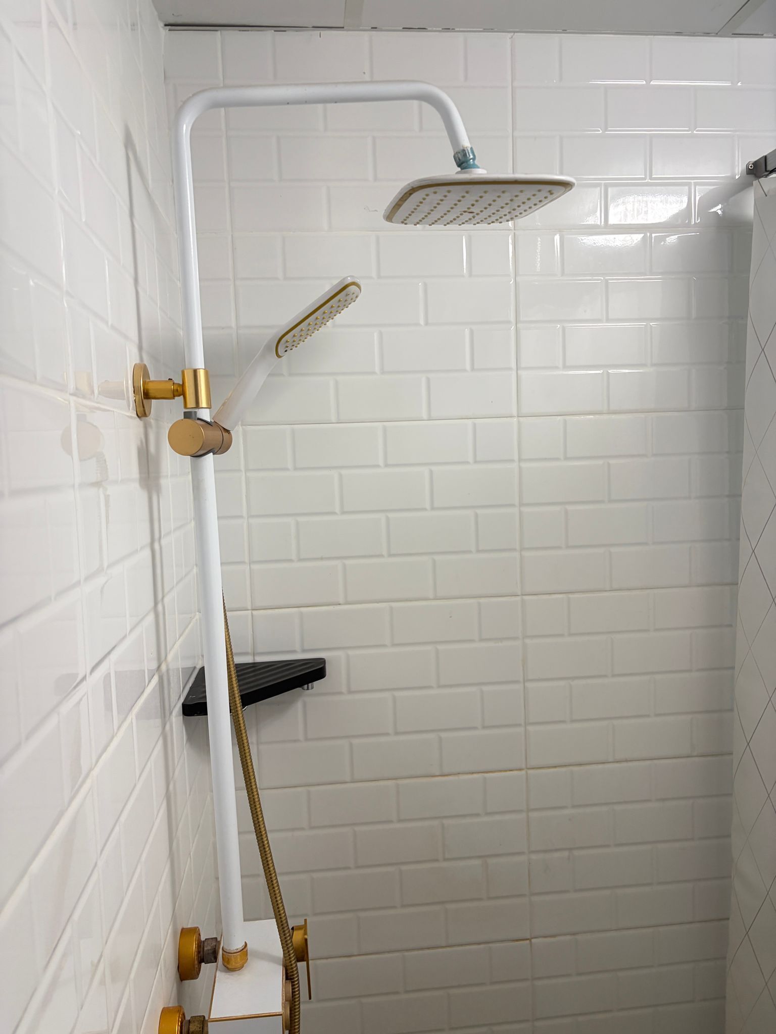 A shower with a handheld showerhead, a wall-mounted control valve, and a black shelf.