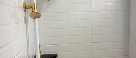 A shower with a handheld showerhead, a wall-mounted control valve, and a black shelf.