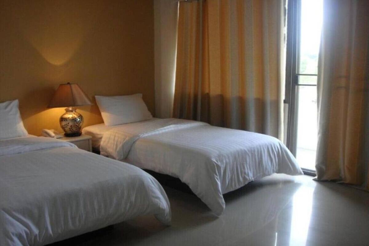 Een hotelkamer met twee bedden, een bedlampje en een raam met gordijnen.