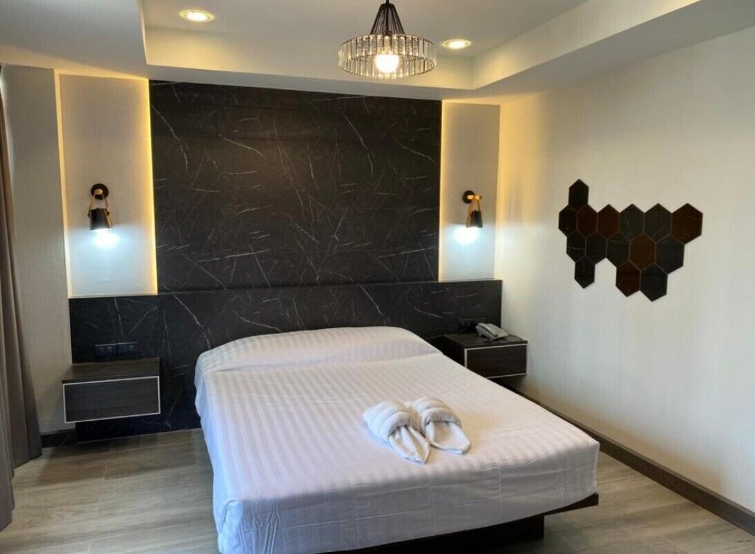 Una habitación de hotel moderna con una cama grande, dos mesitas de noche, un cabecero de mármol oscuro y un adorno de pared geométrico.