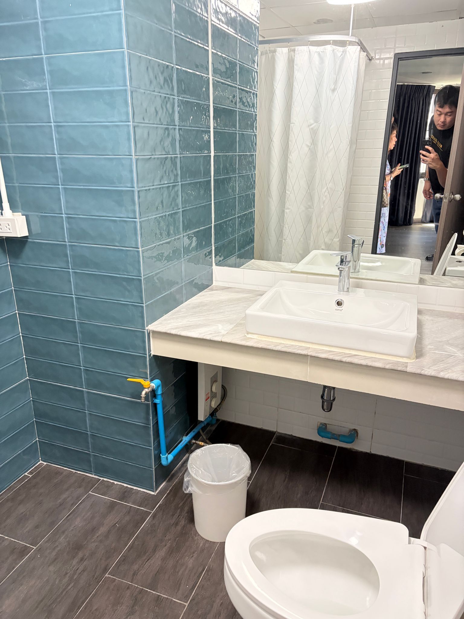 Um banheiro com paredes azulejadas em azul, uma pia branca, um espelho e um vaso sanitário.