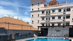 Ein Schwimmbecken mit Hai-Motiven, ein überdachter Bereich mit Stühlen und ein Gebäude mit Balkonen im Hintergrund.