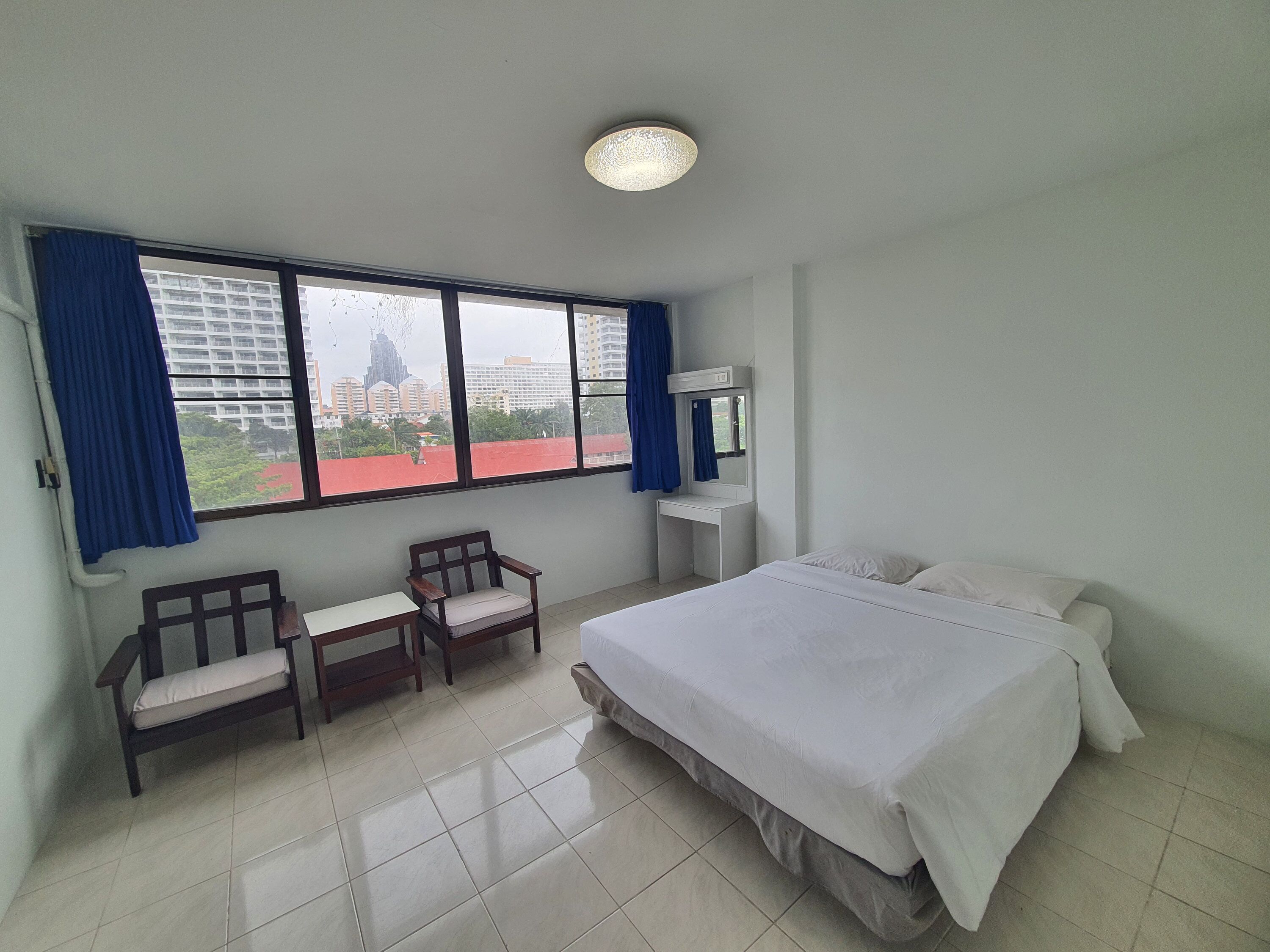 Una habitación de hotel con cama, dos sillas, escritorio, espejo y un ventanal con cortinas.