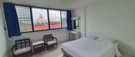 Una habitación de hotel con cama, dos sillas, escritorio, espejo y un ventanal con cortinas.