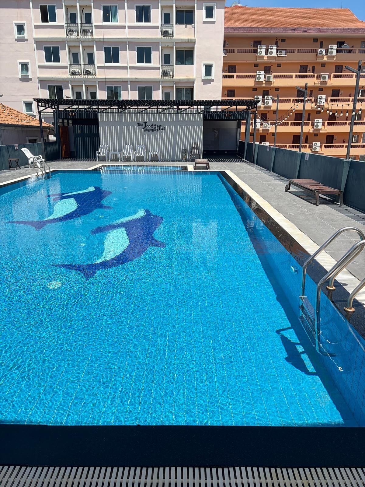 Ein Schwimmbecken mit klarem, blauem Wasser, umgeben von einer Liegefläche mit Liegestühlen und einem Gebäude im Hintergrund.