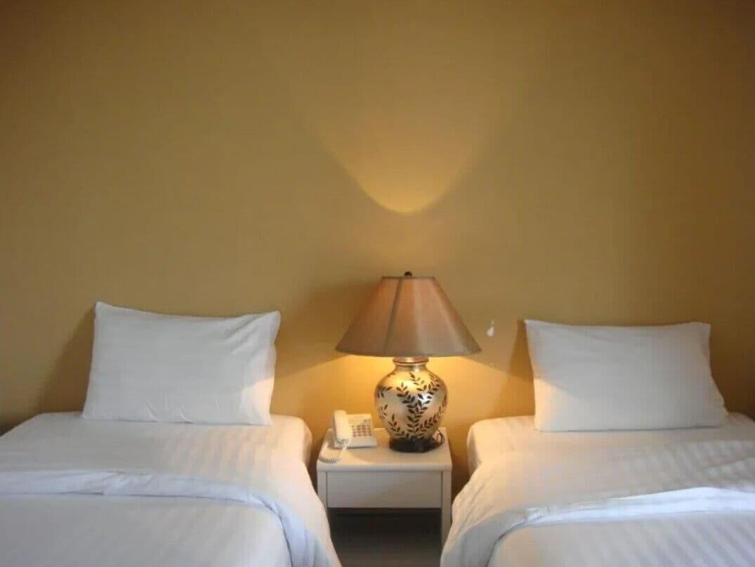 A hotel room with two beds, a nightstand with a lamp, and a phone.