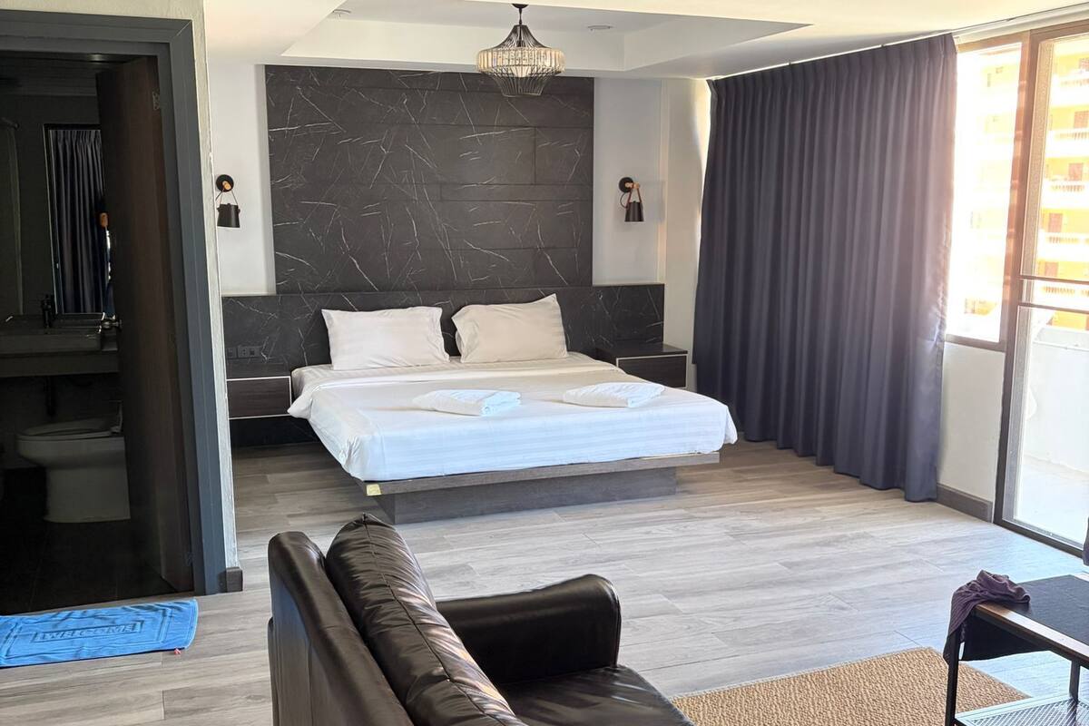 Een moderne hotelkamer met een groot bed, een leren bank, een klein tafeltje en uitzicht op de stad.