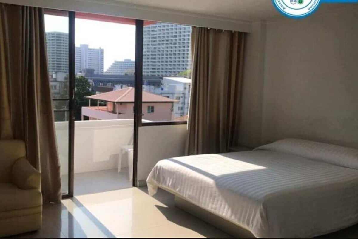 A hotel room with a bed, a sofa, a sliding glass door, and a view of buildings.