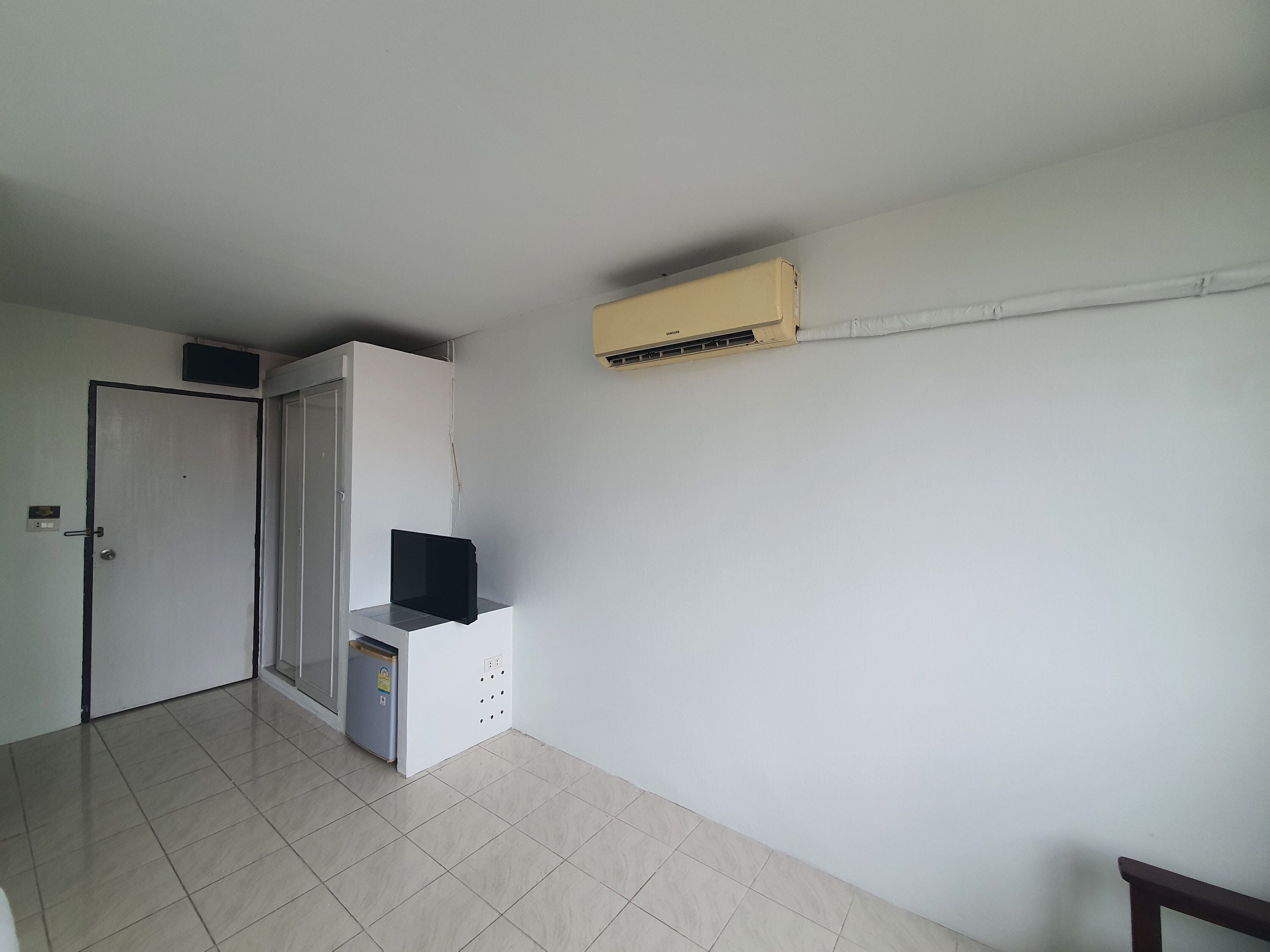 A room with a door, a small cabinet, and an air conditioning unit on the wall.