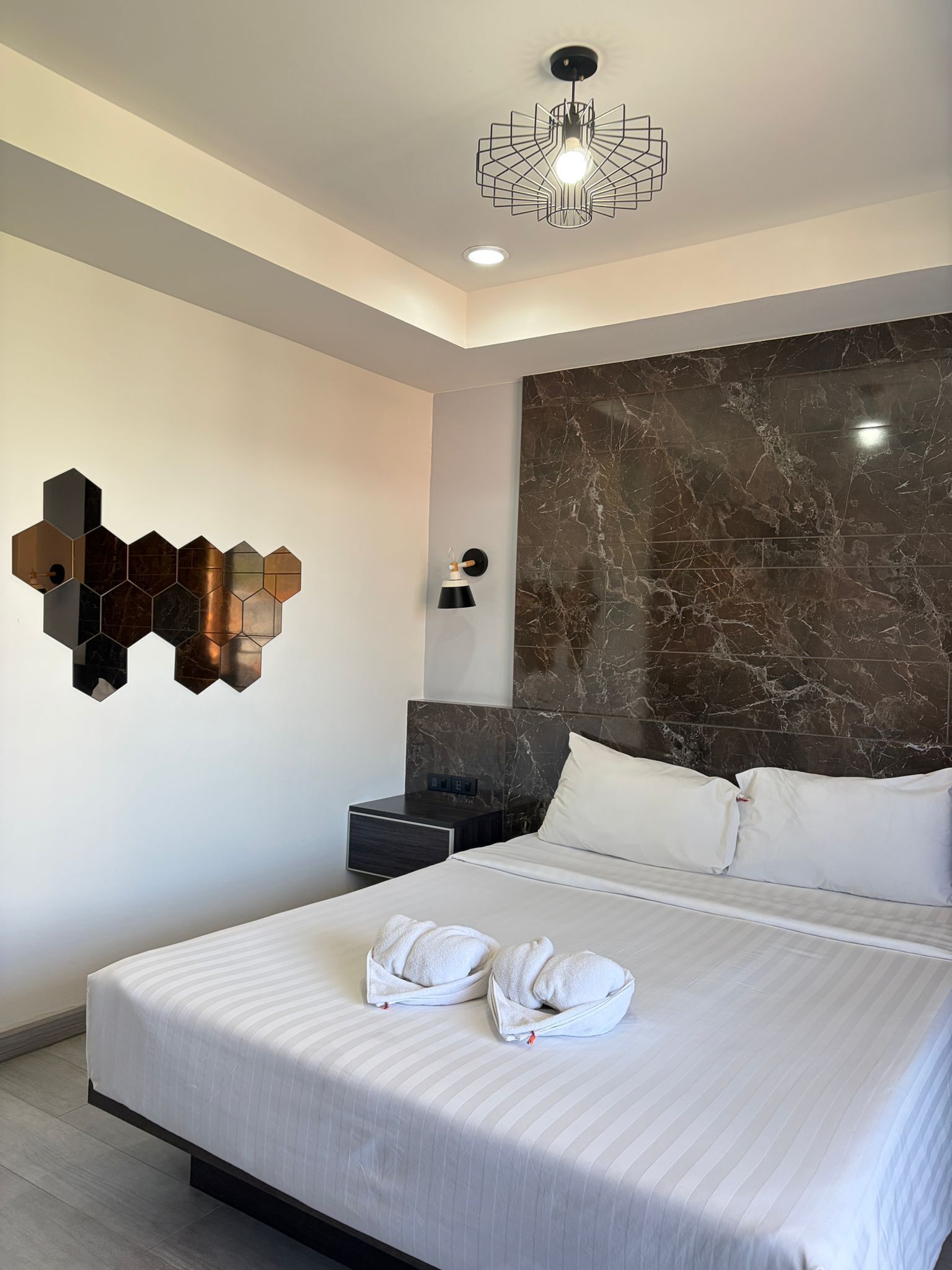 Een moderne hotelkamer met een groot bed, een accentmuur van marmer, een geometrische lamp en een wandlamp.