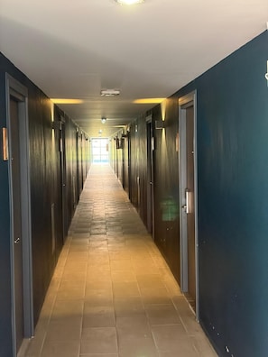 A long, narrow hallway with doors on both sides, leading to a bright room at the end. - Palette Jomtien Longstay (Pattaya)