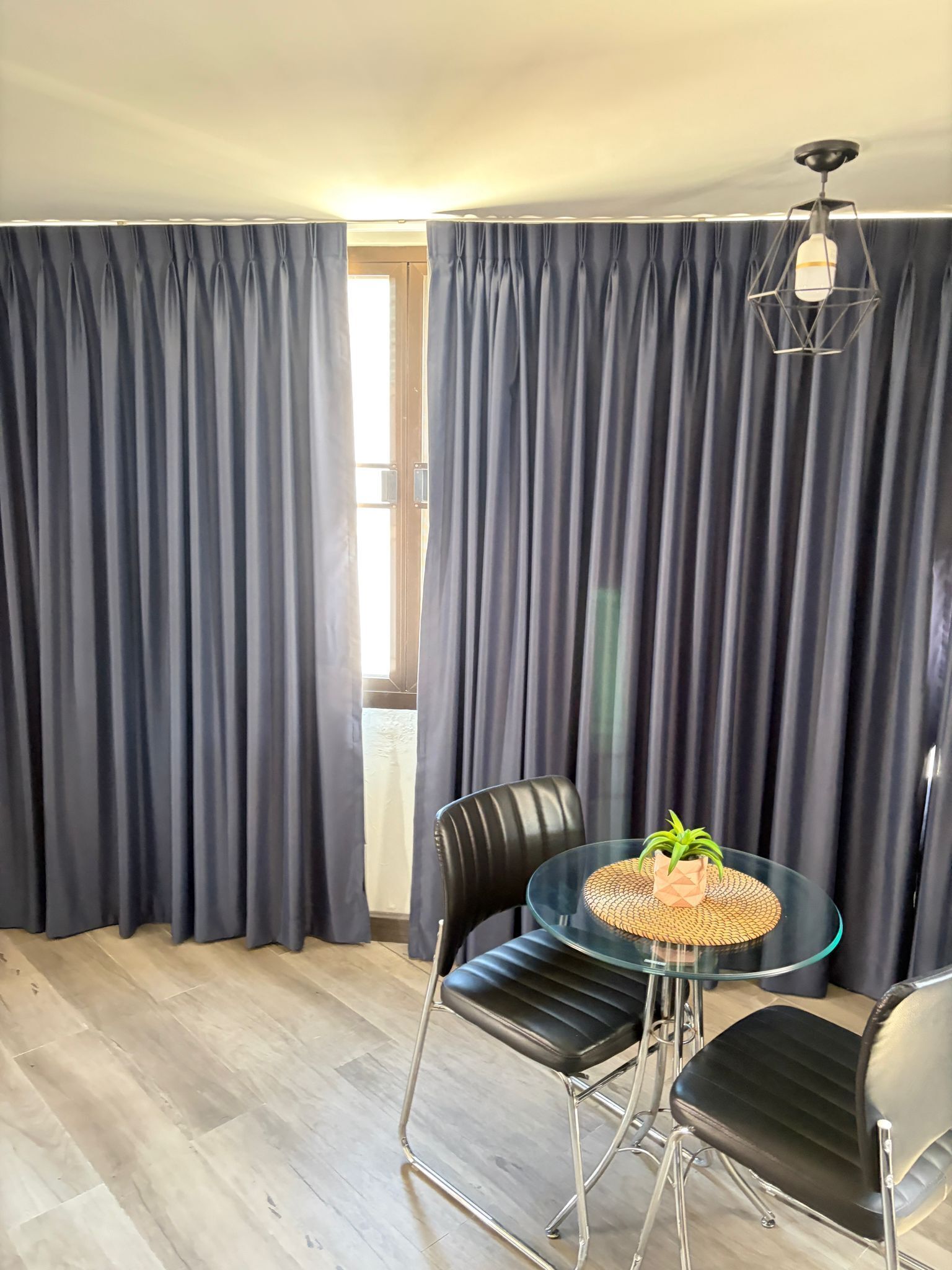 A room with a glass table, two black chairs, a woven placemat, and a ceiling light fixture.