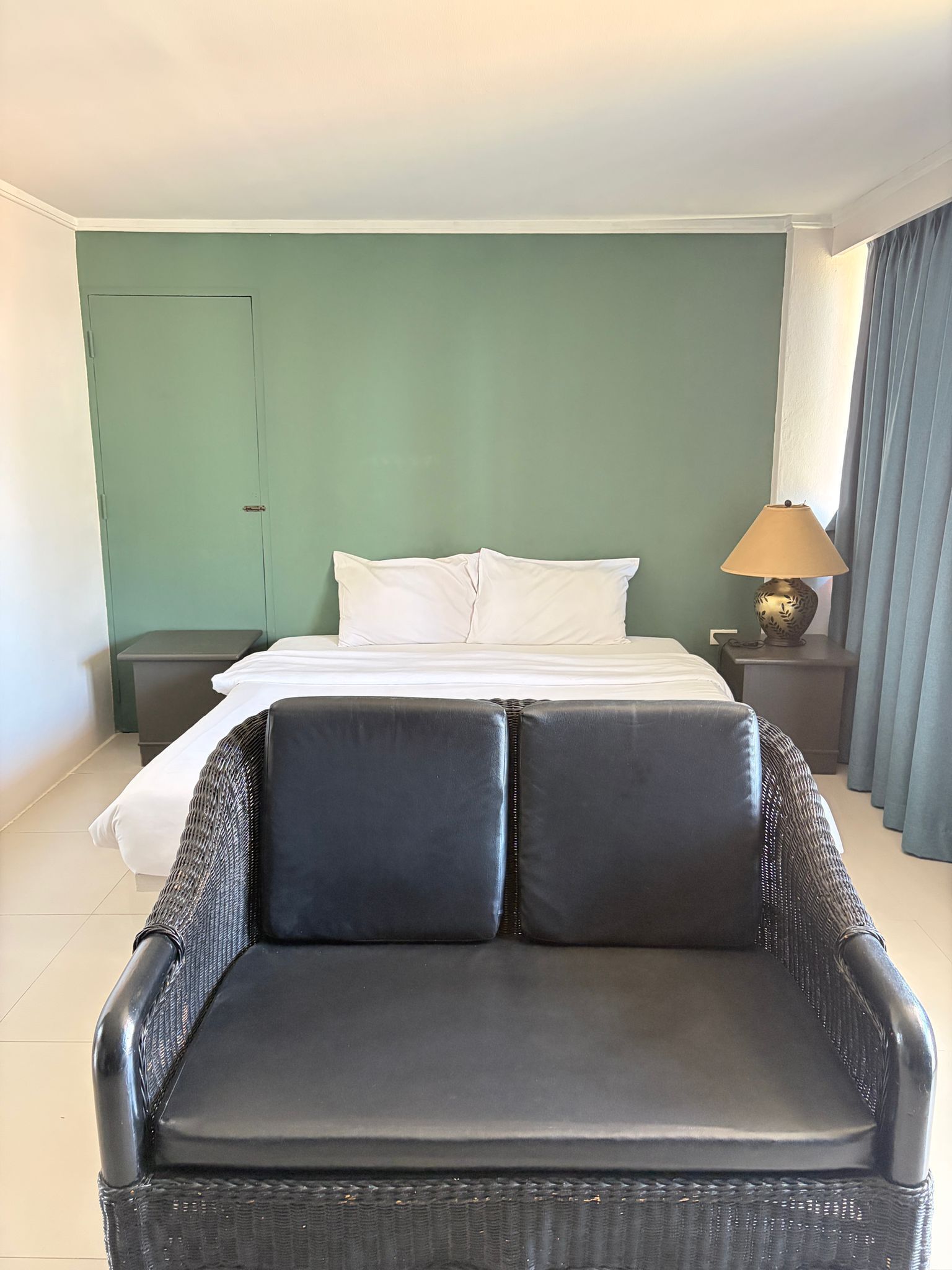 Una habitación de hotel con cama, mesita de noche, lámpara, silla y puerta.