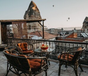 Un balcón con sillas de mimbre y una mesa, con vistas a un paisaje urbano que incluye formaciones rocosas y edificios.