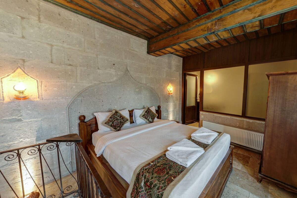 Une chambre à coucher avec un lit en bois, une table de chevet, une armoire, un mur en pierre et une fenêtre donnant sur un paysage agréable.