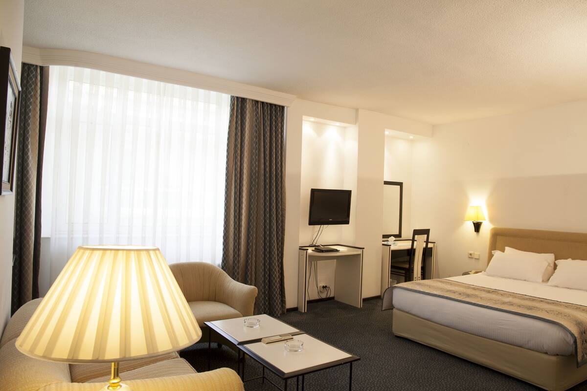 Habitació d'hotel amb un llit, una taula de treball, una cadira, una làmpada i una televisió.
