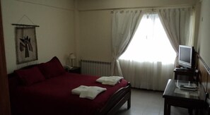 A hotel room with a bed, a desk with a television, and a window with curtains.