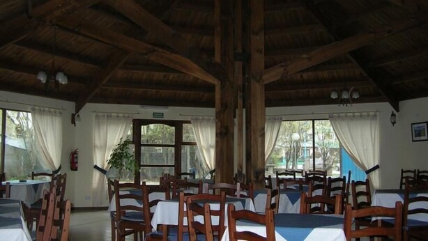 A dining area with wooden tables and chairs, large windows with curtains, and a high wooden ceiling. - Apart Hotel Tierra del Fuego (Ushuaia)
