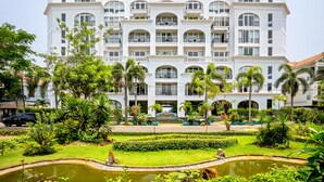 A multi-story hotel with a symmetrical facade, balconies, and a central garden with a pond. - Lasenta Boutique Hotel Hoian (Da Nang)
