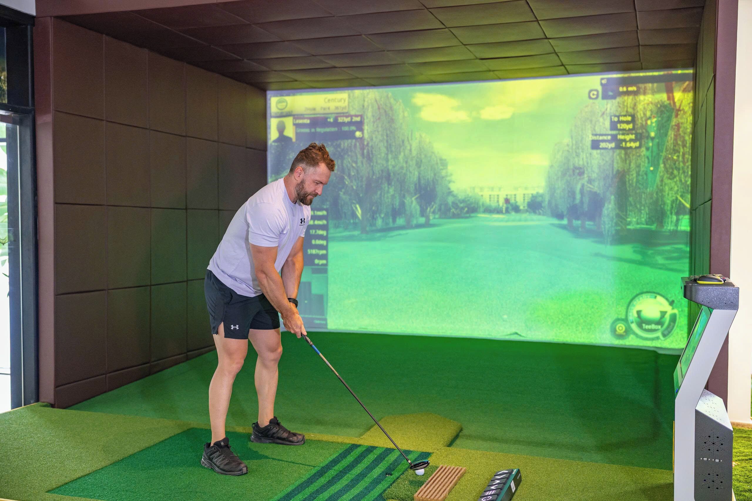 A man practicing golf in a simulated environment with a digital screen displaying a golf course.