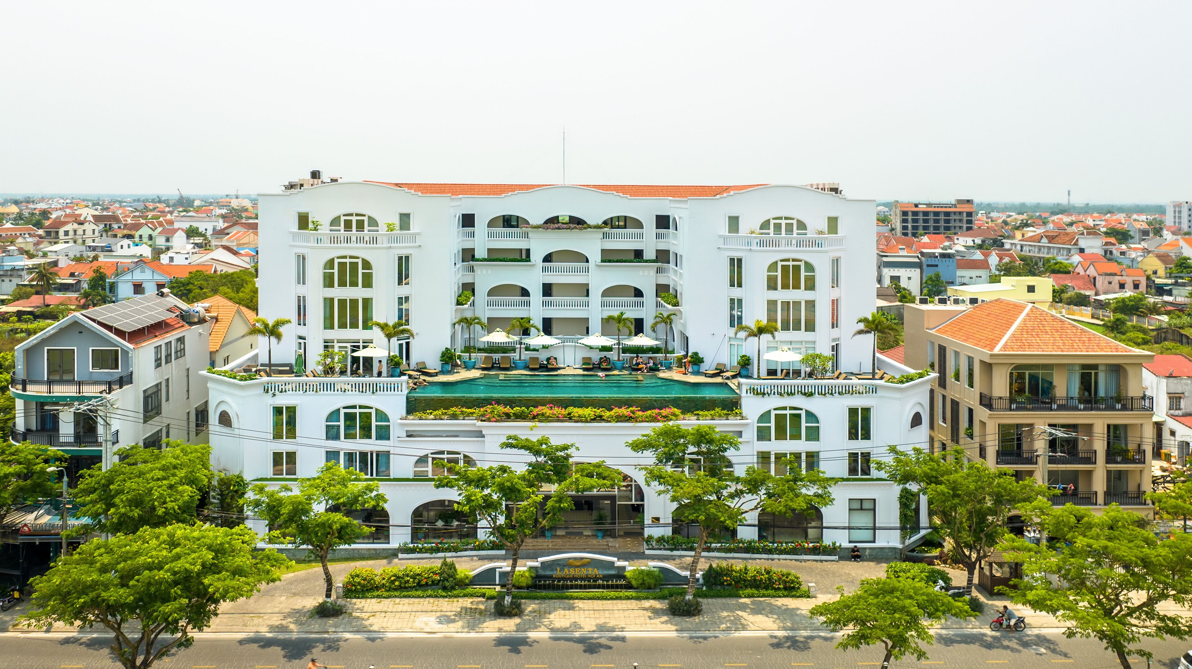 A large hotel with multiple balconies, a swimming pool, and a well-maintained garden.