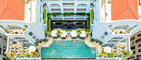 Vue aérienne d’un hôtel doté d’une piscine centrale, entourée d’espaces de détente en plein air et de verdure.