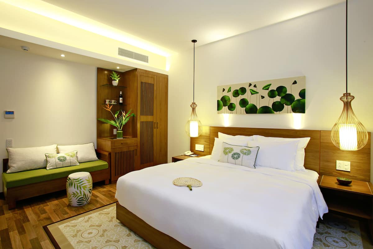 Une chambre d’hôtel avec un grand lit, un canapé vert, une armoire en bois et une plante fixée au mur.