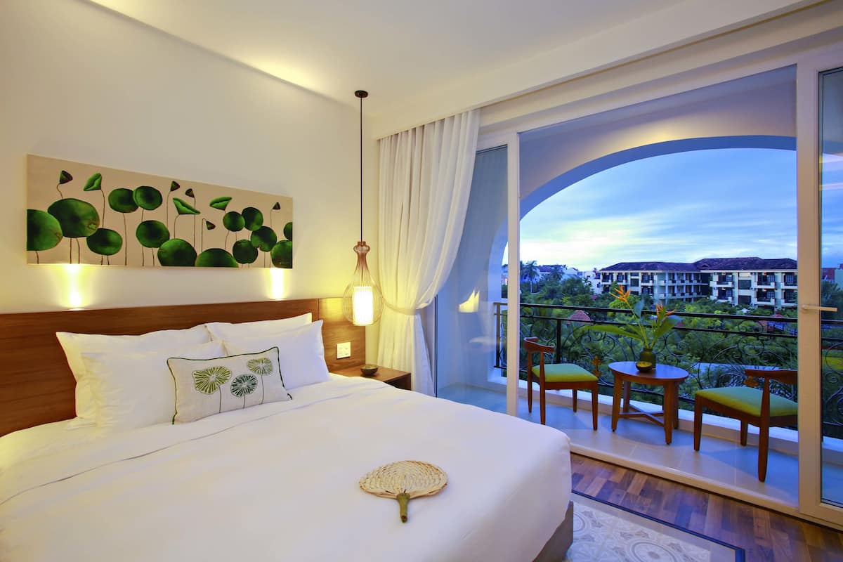 Une chambre d’hôtel avec un grand lit, un balcon avec des chaises et une vue sur les immeubles.