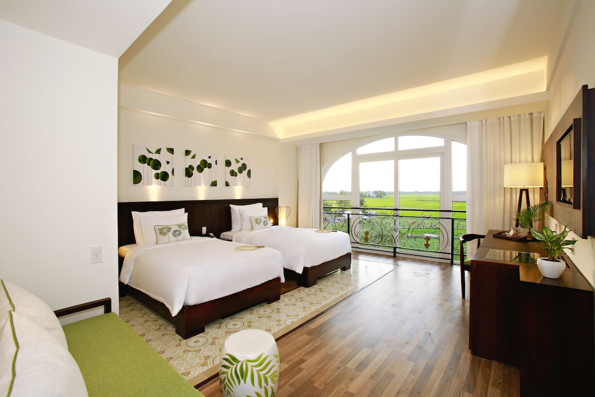 Une chambre d’hôtel avec deux lits, un balcon offrant une vue agréable et un coin repas avec une table et des chaises.