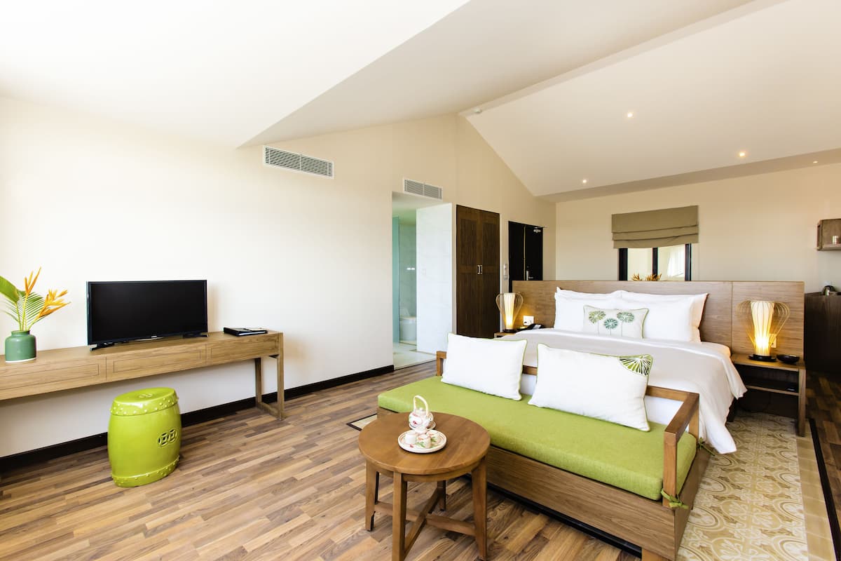 Une chambre d’hôtel moderne équipée d’un lit, d’une télévision, d’une petite table et d’un tabouret vert.