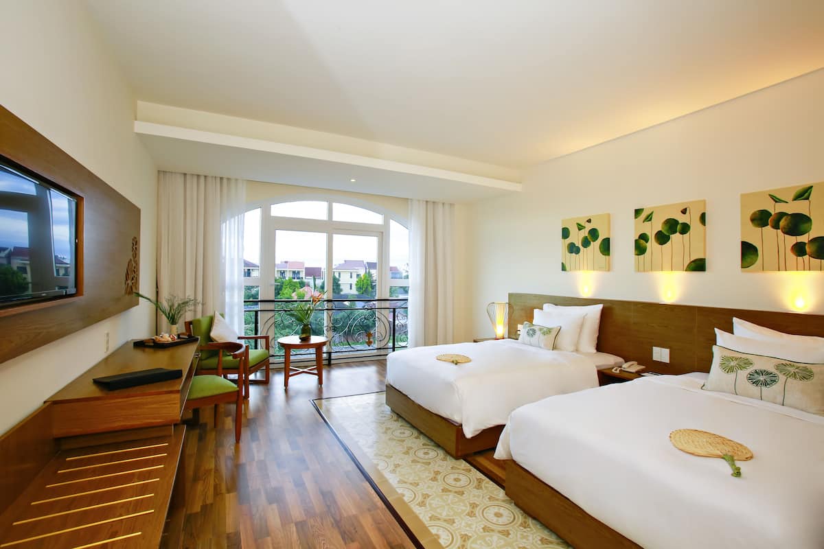 Une chambre d’hôtel avec deux lits, un bureau, une chaise, une télévision et un balcon avec vue.